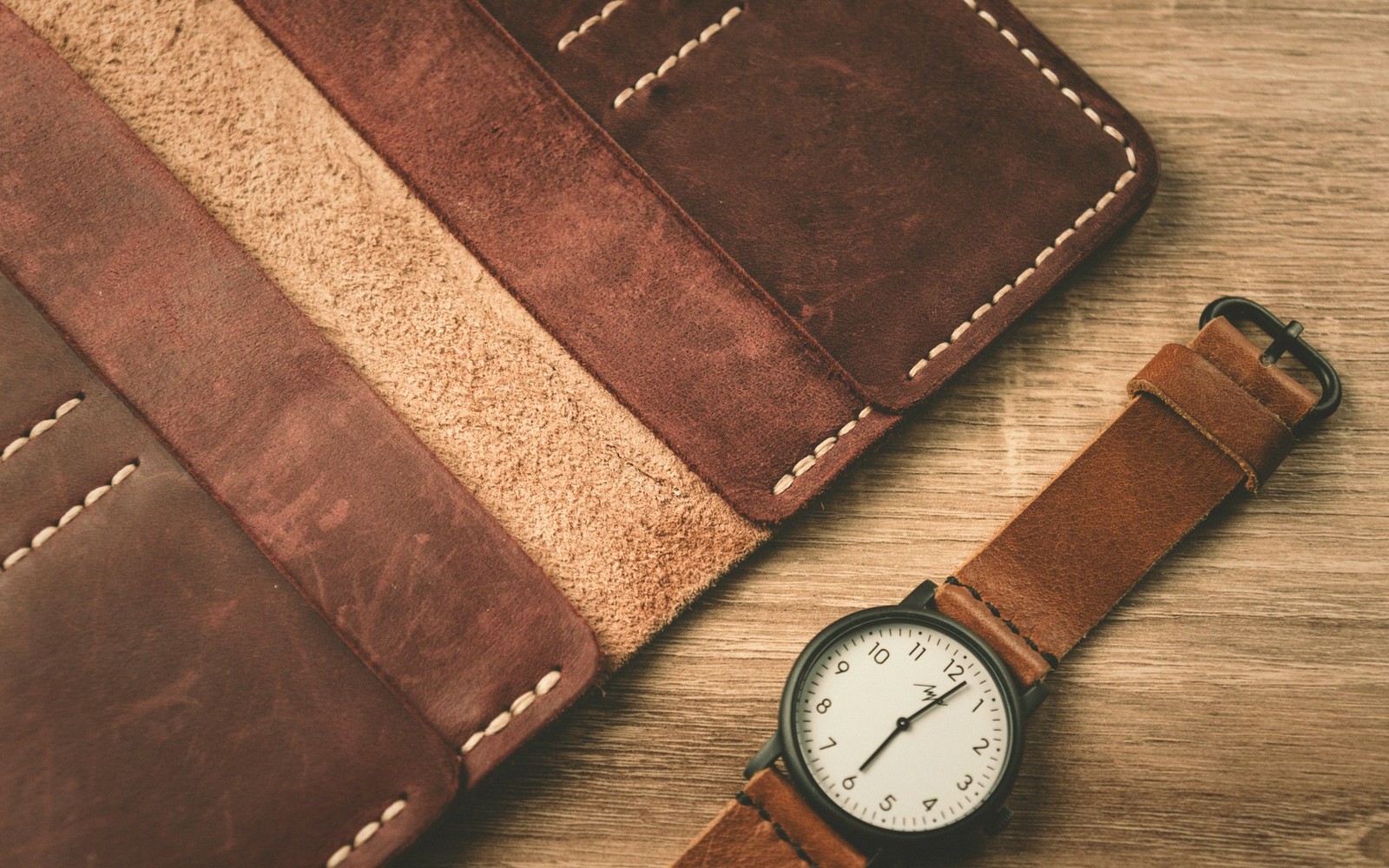 Open brown leather wallet with stitched panels beside a wristwatch with a leather strap