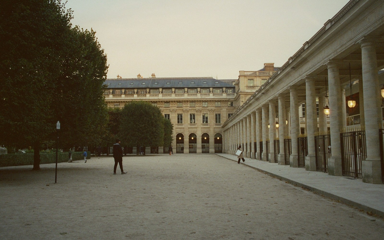 Colonnaded courtyard of a Parisian palace with pedestrians walking across the gravel square