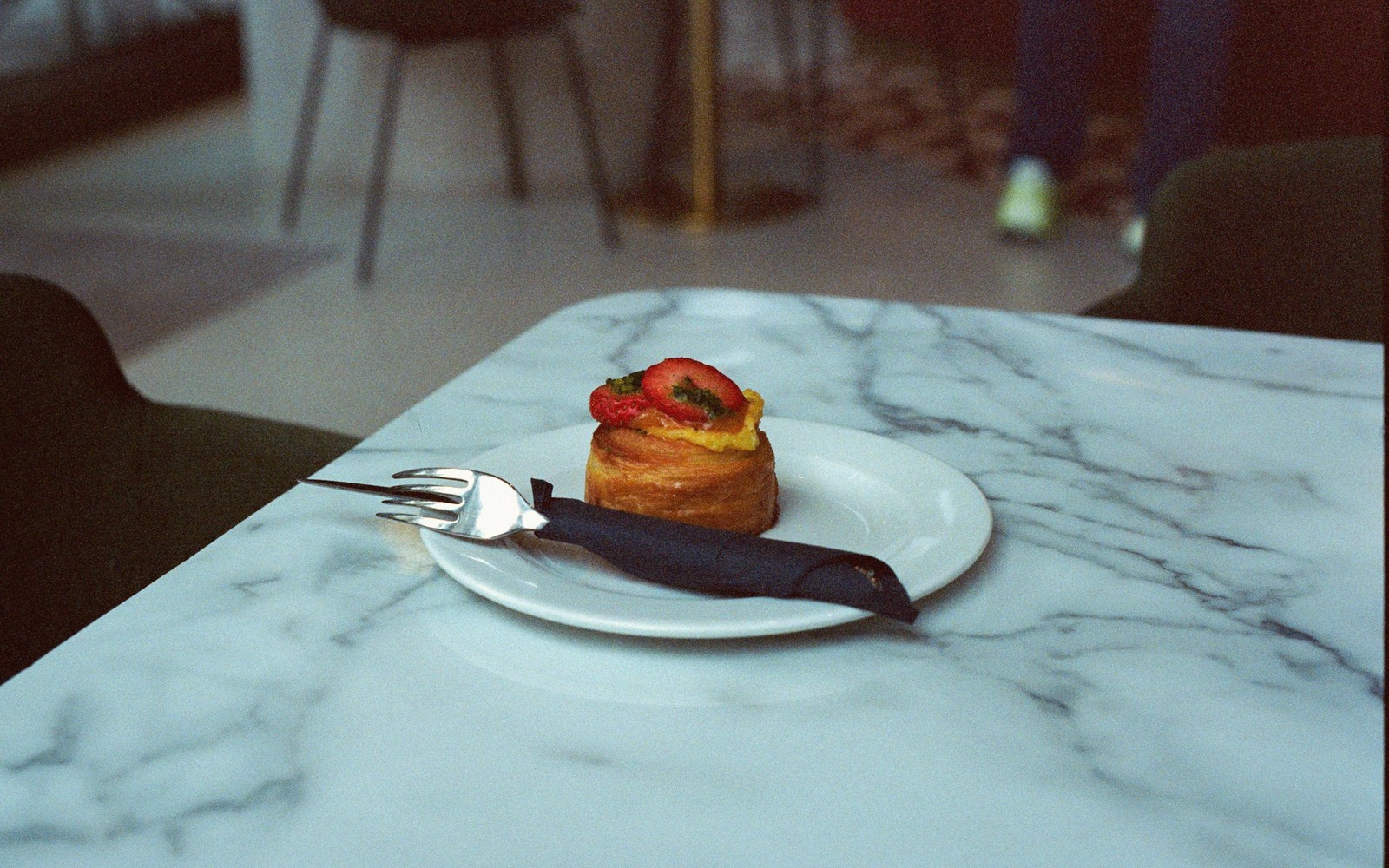 A pastry topped with strawberry and custard sits on a plate at a marble table